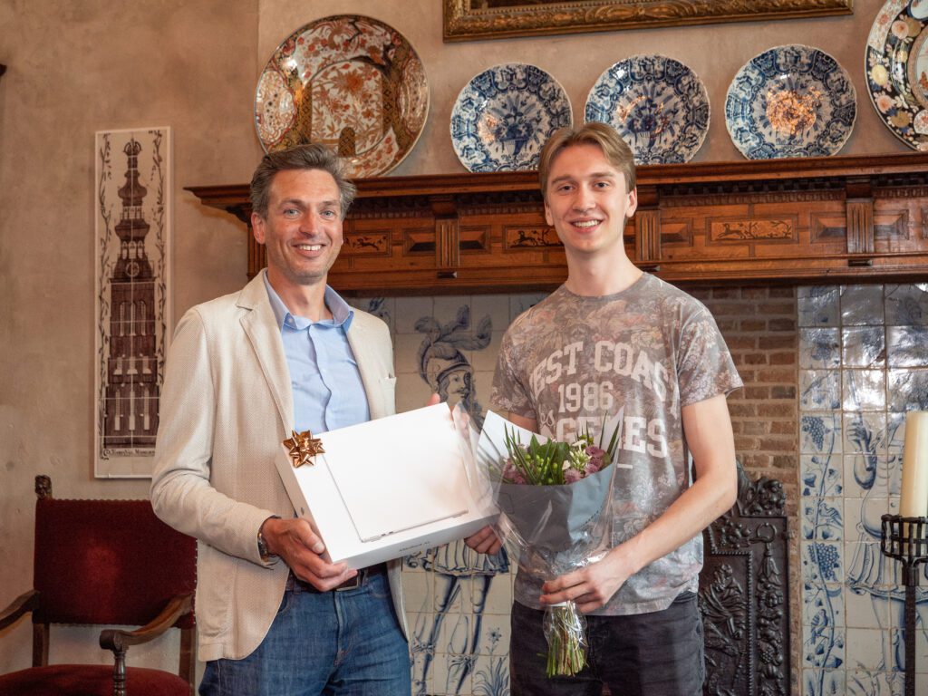 Tablet-38 Olof (links) overhandigt een prijs en bloemen aan Daniël (rechts), die glimlachend poseert in een klassiek ingerichte kamer